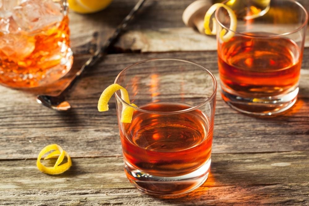 2 glasses of Sazerac Cocktail with lemon peel on wooden table