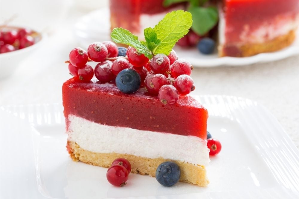Piece of cheesecake with jelly berry and berry fruits on top on a white plate.