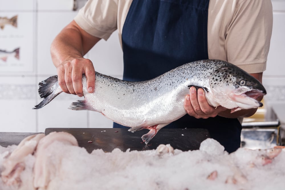 Fish monger holding a whole pink salmon at the market