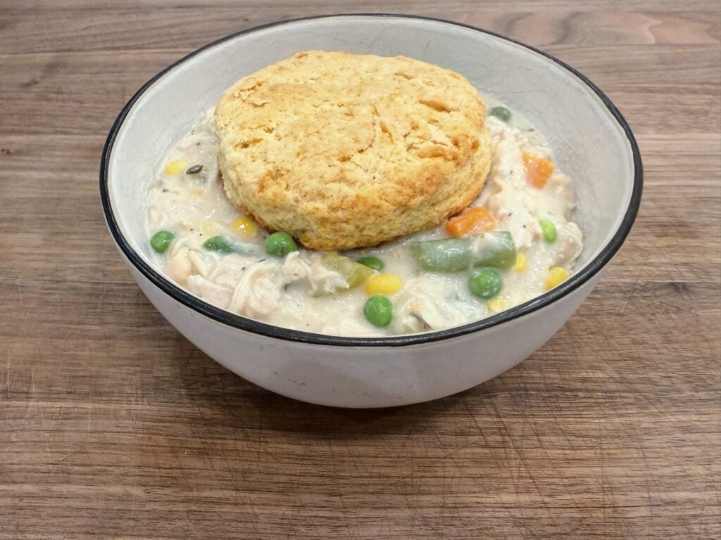 Chicken pot pie filling in a bowl with a biscuit on top