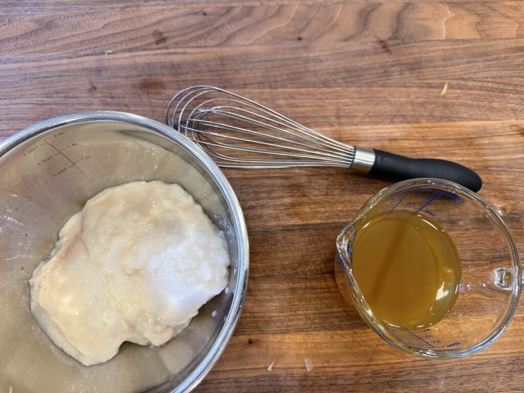 Cream of chicken soup in a bowl with chicken broth and a whisk