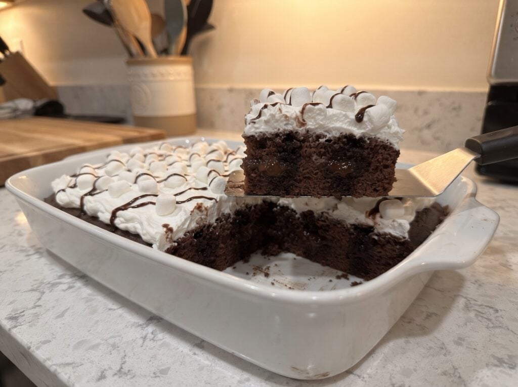 Hot chocolate poke cake with whipped topping, mini marshmallows and chocolate drizzle