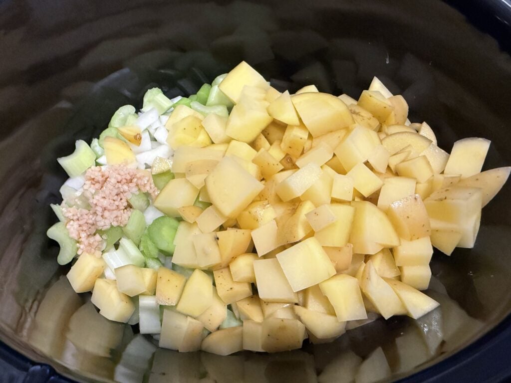 Diced potatoes, celery, onion and garlic in the bottom of a slow cooker